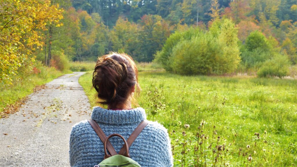 Frau blickt auf einen Pfad und auf eine grüne Wiese. Wege aus dem Burnout. Wie kann man das ausgebrannt sein überwinden?