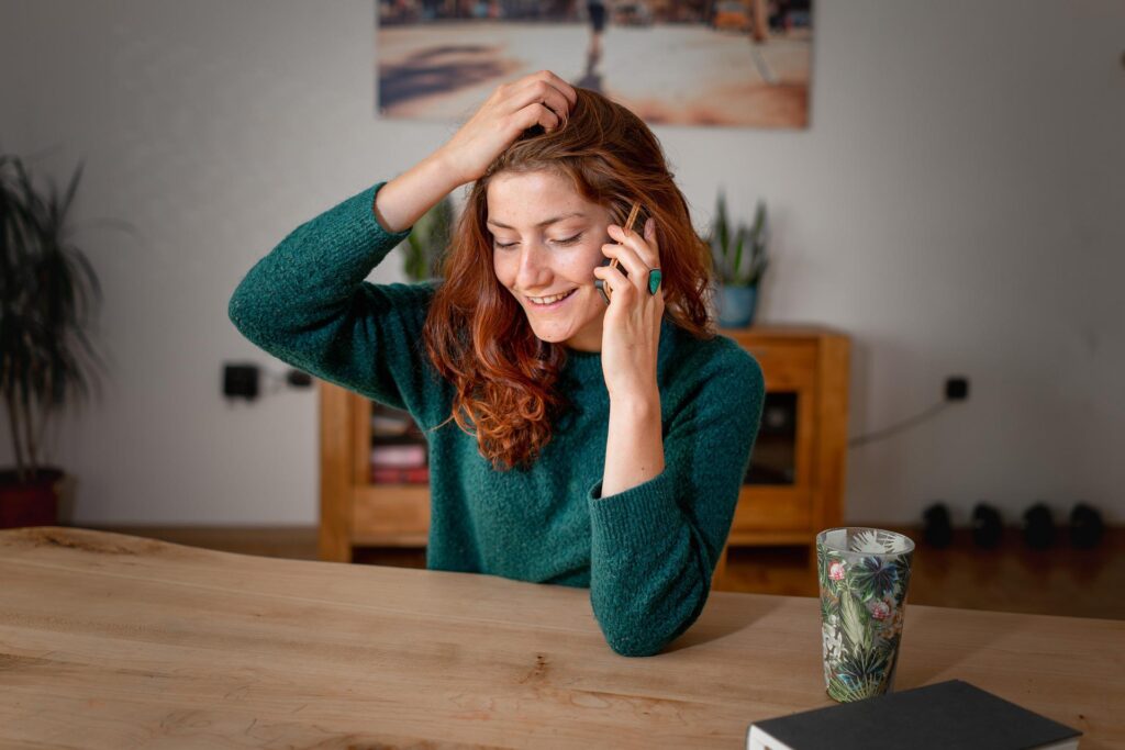 Frau sitz fröhlich am Esstisch und telefoniert. Nehmen Sie Kontakt mit uns auf.