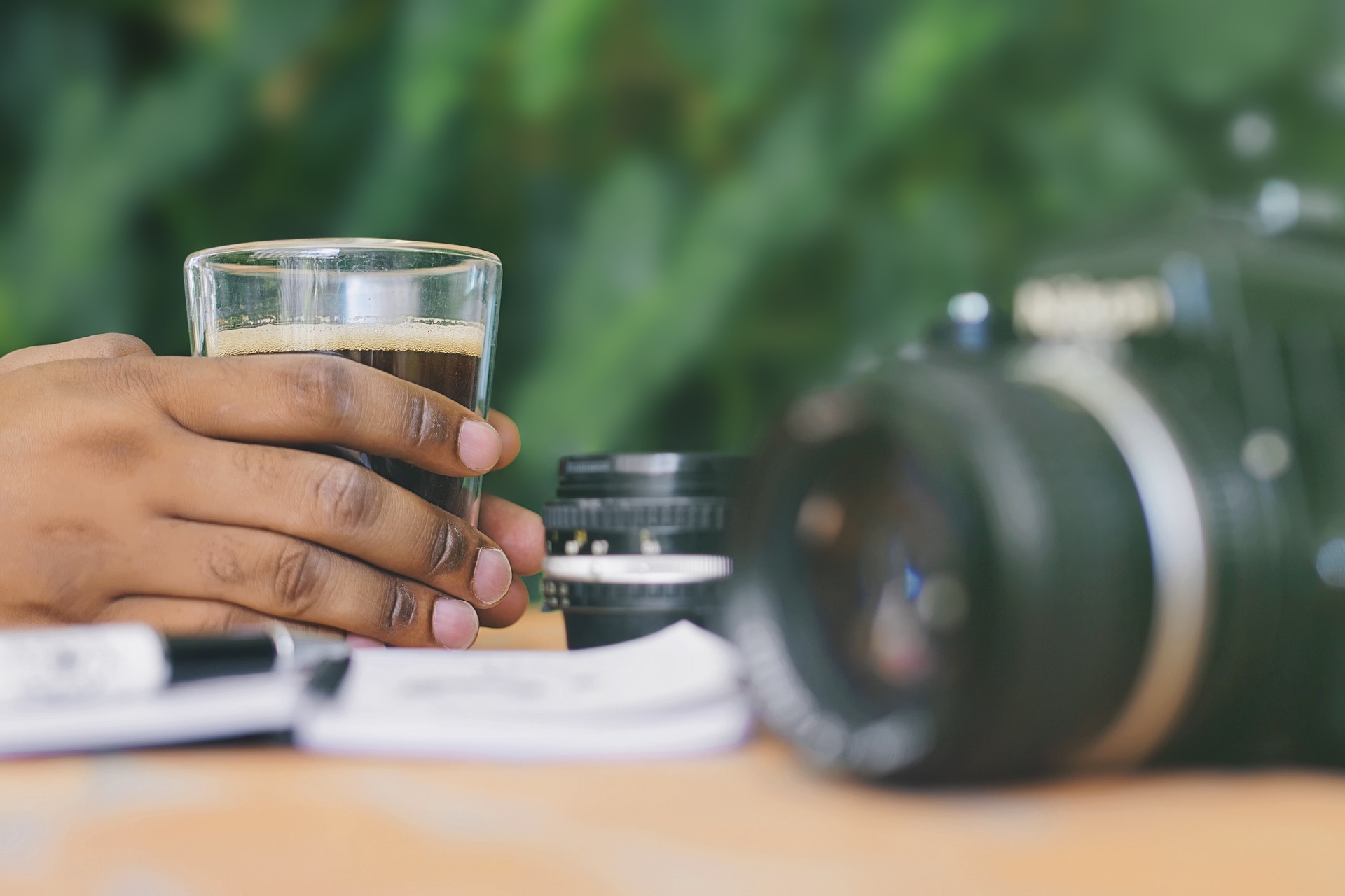 Ein Mann hält eine Kaffeetasse und sitzt an einem Tisch. Im Hintergrund sieht man seine Fotokamera. Pausen sind reizend, weil sie uns entspannen und neue Gedanken ermöglichen.