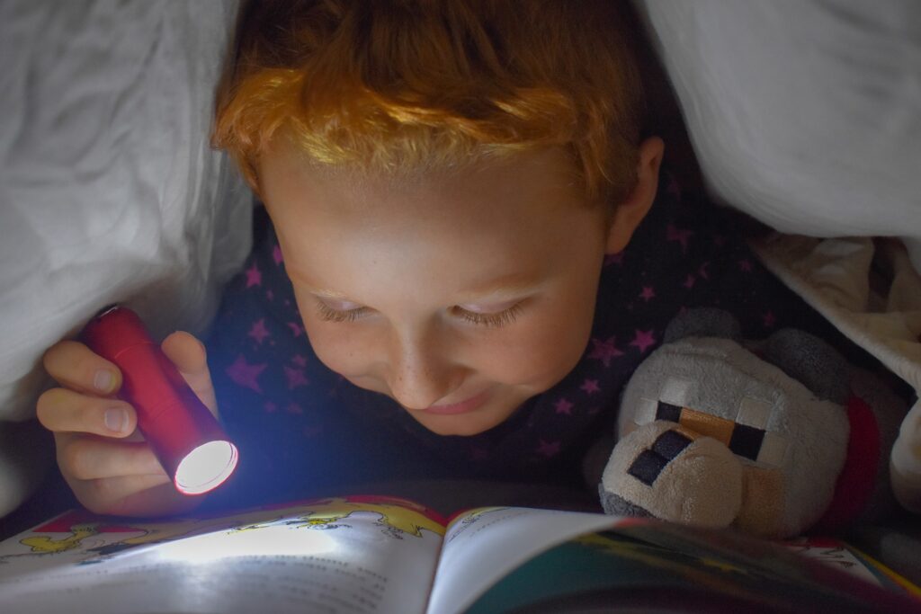 Zum lesen verführt. Kind liest heimlich unter einer Decke mit seiner Taschenlampe.
